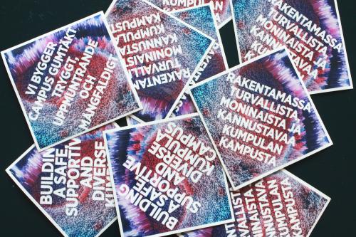 Lappuja, joissa eri kielillä teksti "Rakentamassa turvallista, moninaista ja kannustavaa Kumpulan kampusta".