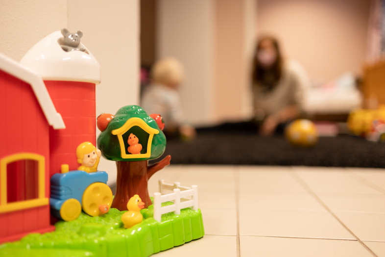 In the picture are children's toys and a parent and a child playing in the background.