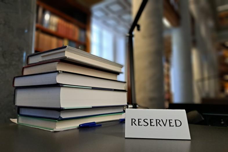 A pile of books and a sign that reads "Reserved" on a desk.