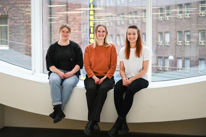 Trepersonerslaget Three Mushketeers sitter framför Kaisa-husets fönster.