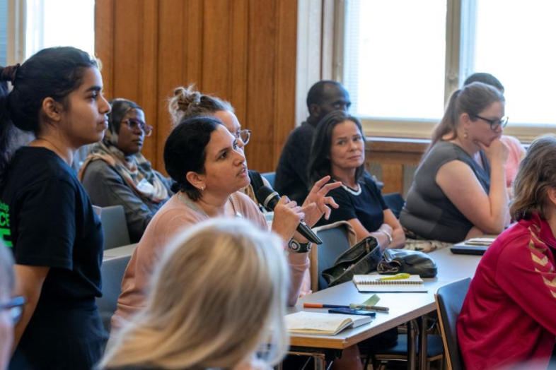 En grupp människor sitter i en föreläsningssal. I mitten en person som pratar i en mikrofon.