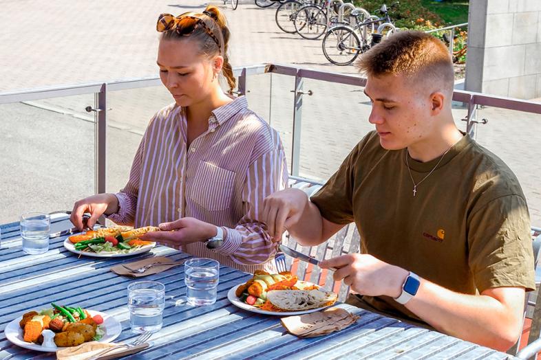 Två personer äter Unicafe-lunch utomhus.