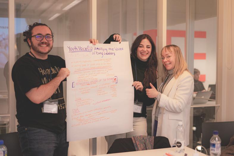 Three students are smiling and holding up a poster with their idea written on it