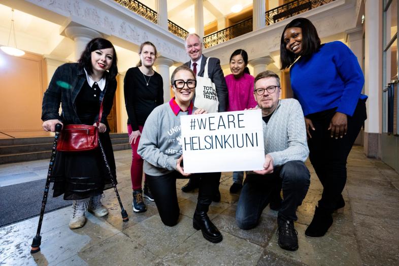 University community members in the lobby of the main building with the #wearehelsinkiuni sign.