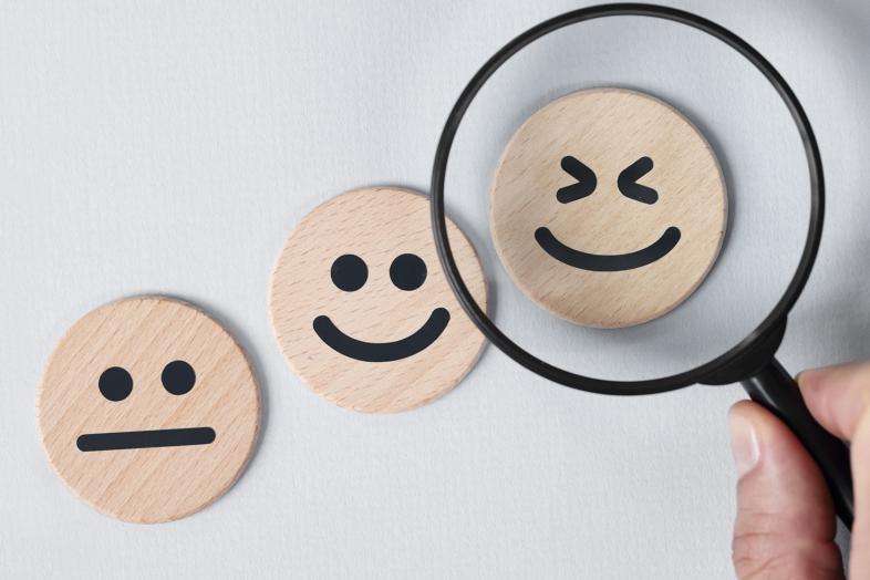 Tre leende träklossar och ett förstoringsglas som visar den bredaste leende träklossen.