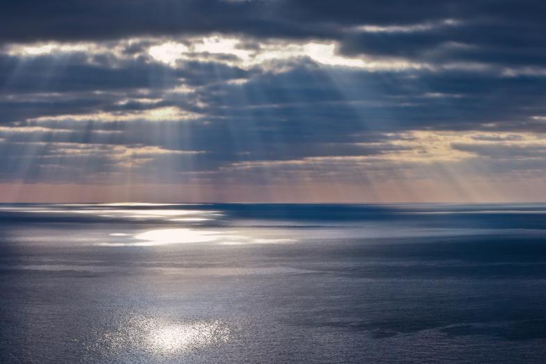 Auringon valonsäteitä pilvien raoista meren yllä.