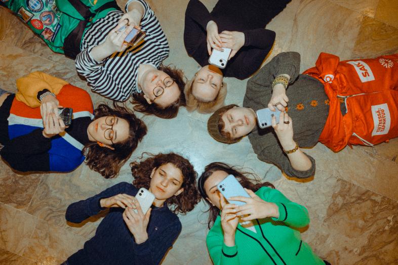 Opiskelijat makaavat lattialla puhelimet kädessä.