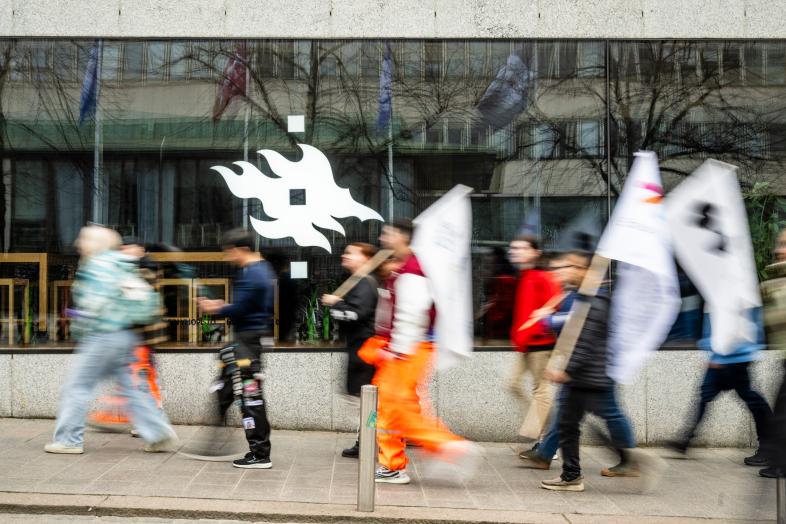 Etualalla opiskelijoita, taustalla Tiedekulman ikkunat ja yliopiston liekkimerkki.