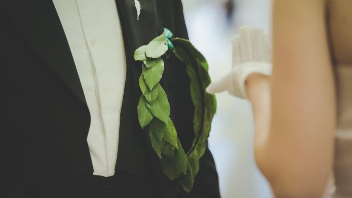 A wreath bound to a tailcoat and a hand dressed in a white glove.