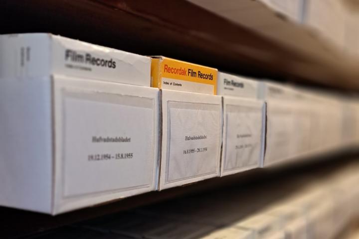 Keltainen mikrofilmilaatikko valkoisen laatikkorivin keskellä.